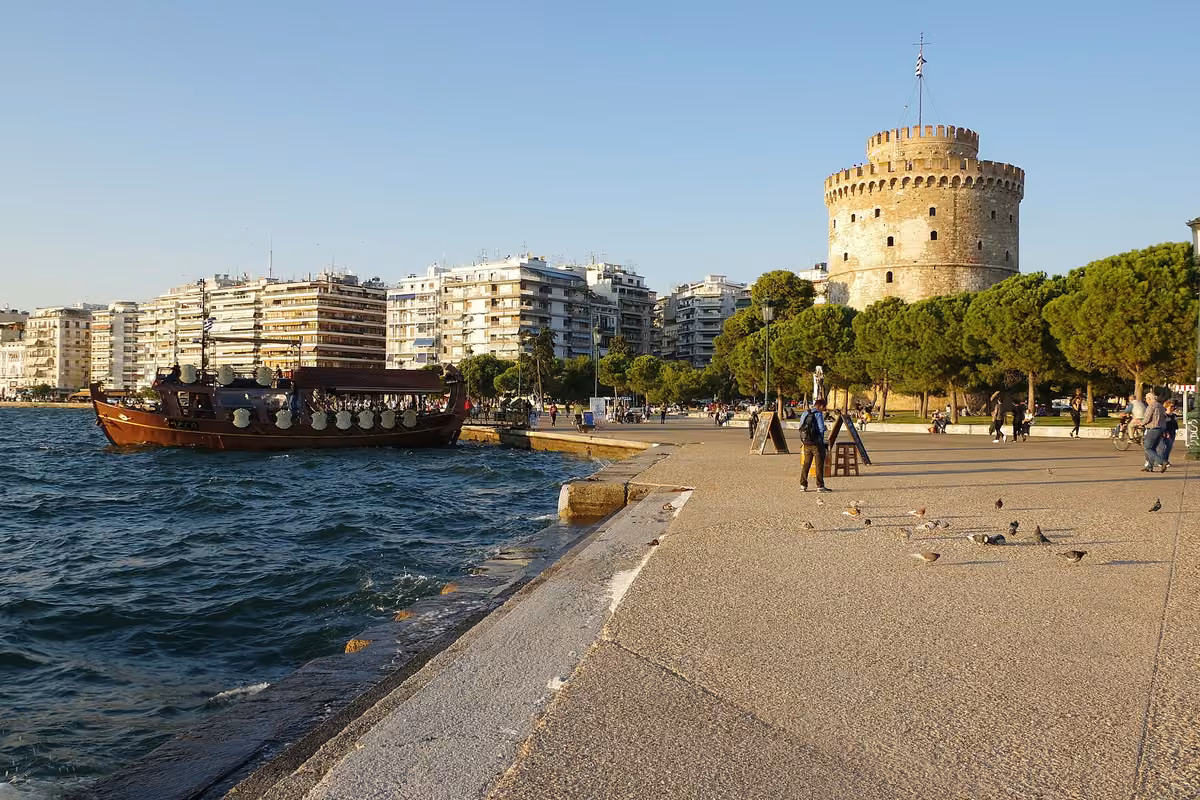 A round stone tower at the end of a wide seafront promenade, a wooden boat moored alongside