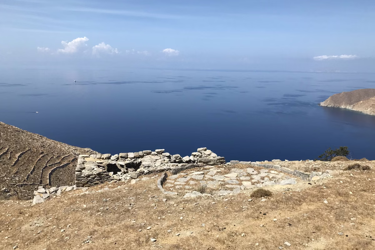 A ruined stone hut and old terraces on a dry hillside above a calm, wide blue sea