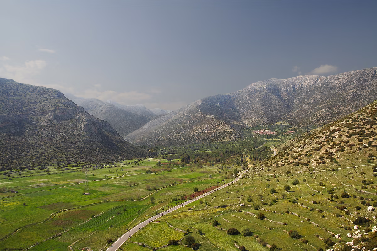 A green plain of small fields between bare rocky mountains, with a road running along its edge