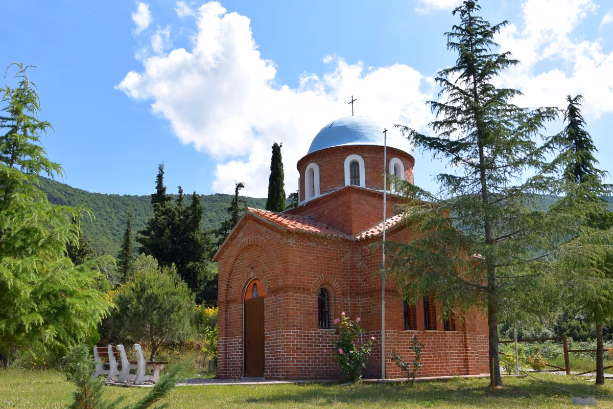 A red-brick chapel with a blue dome among cypresses and pines