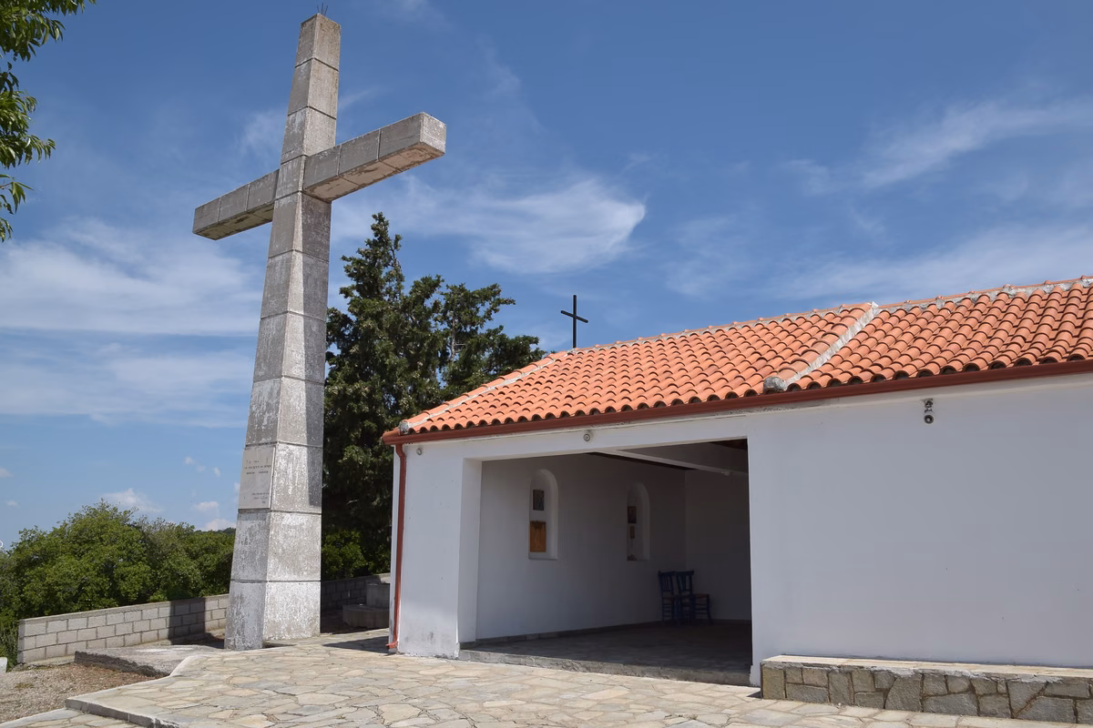 A large white stone cross beside a small whitewashed chapel with a red roof