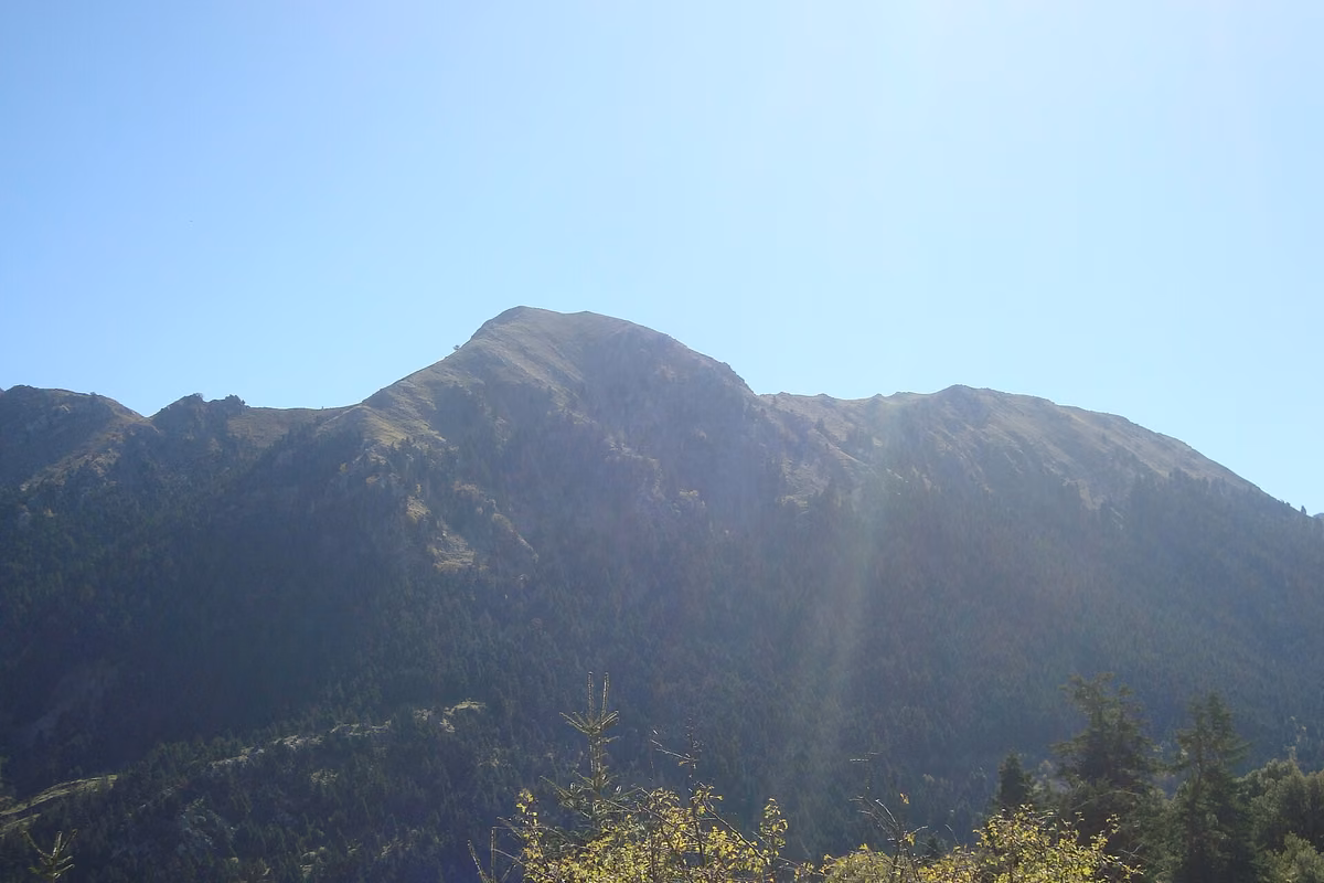 A wooded summit of the Lampeia range against a bright blue sky