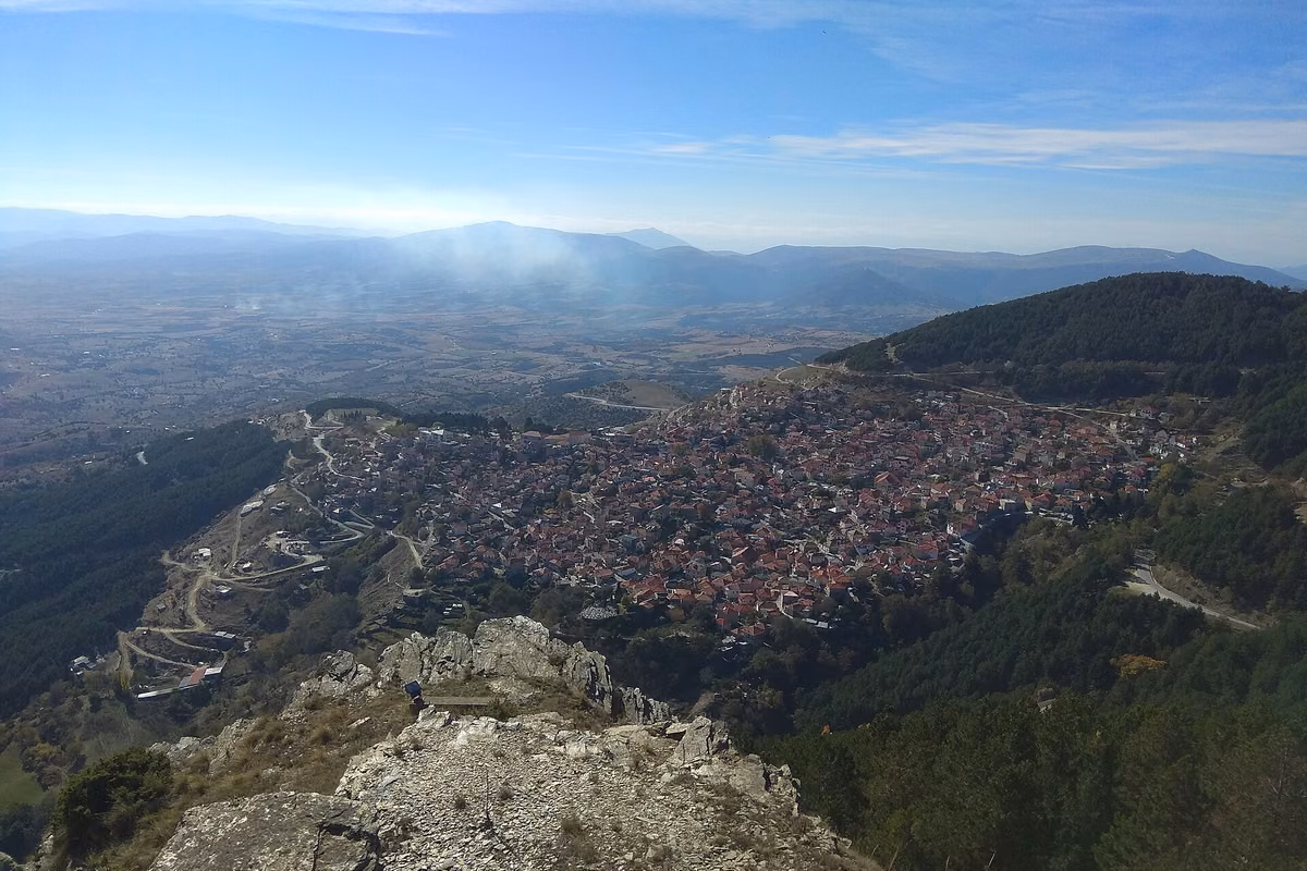 A village of red roofs below a rocky viewpoint, with a wide plain and low hills beyond