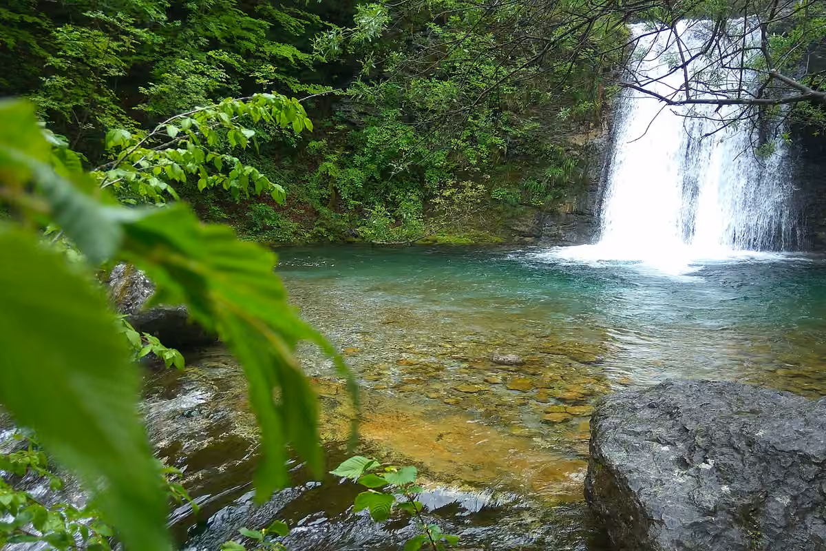A waterfall dropping into a clear green pool in the Enipeas gorge