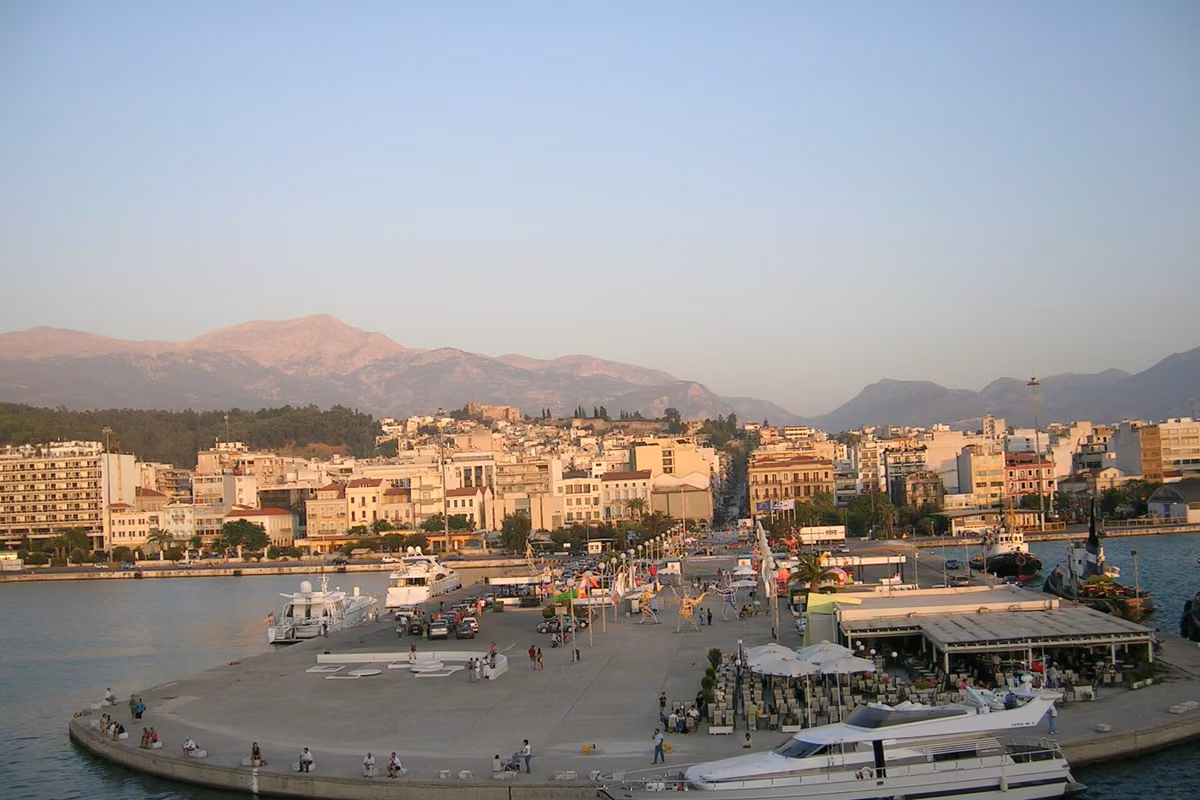 A harbour front with a pier and moored boats, the town and mountains behind at dusk