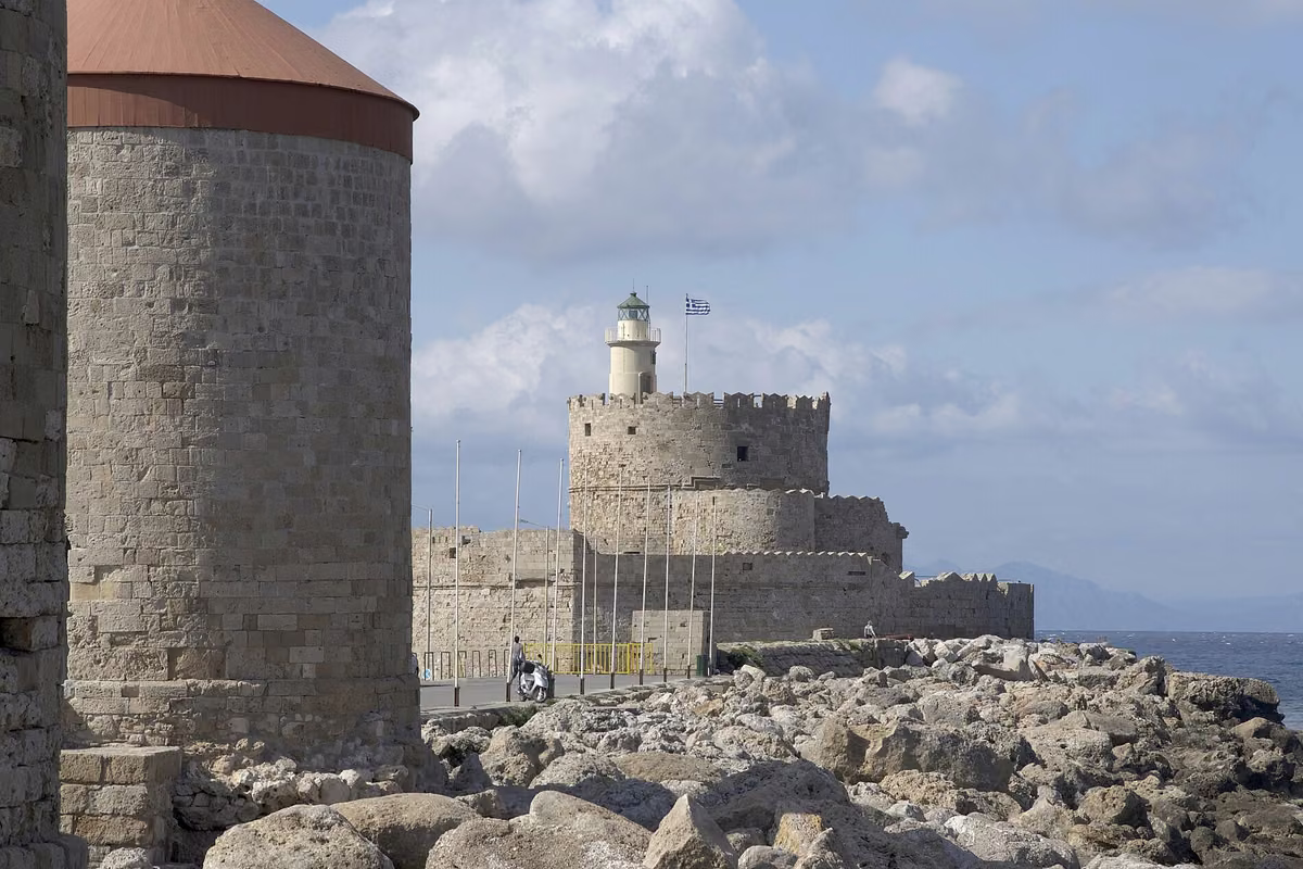 A stone windmill beside a rocky mole, with a round fort and lighthouse beyond